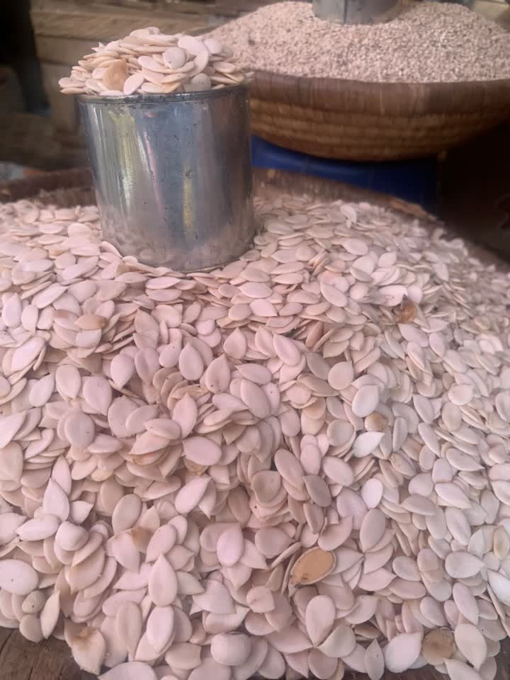 A basket heaped with pale egusi melon seeds beside a metal measuring cup